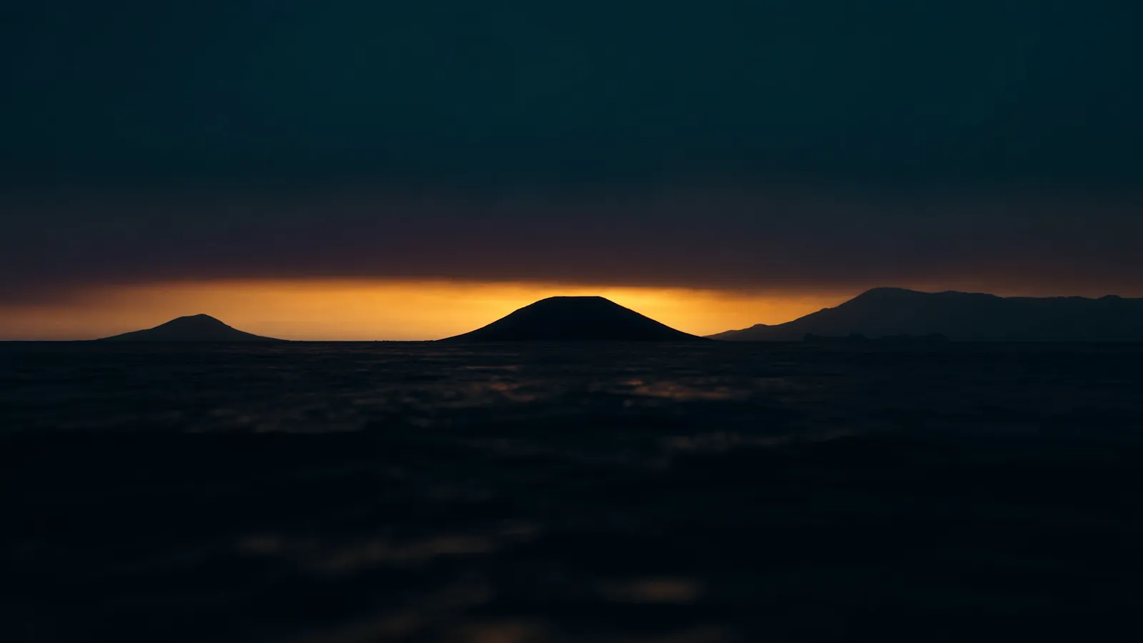 Visualización artística de un cono volcánico recortado contra una franja dorada de amanecer sobre el mar en calma