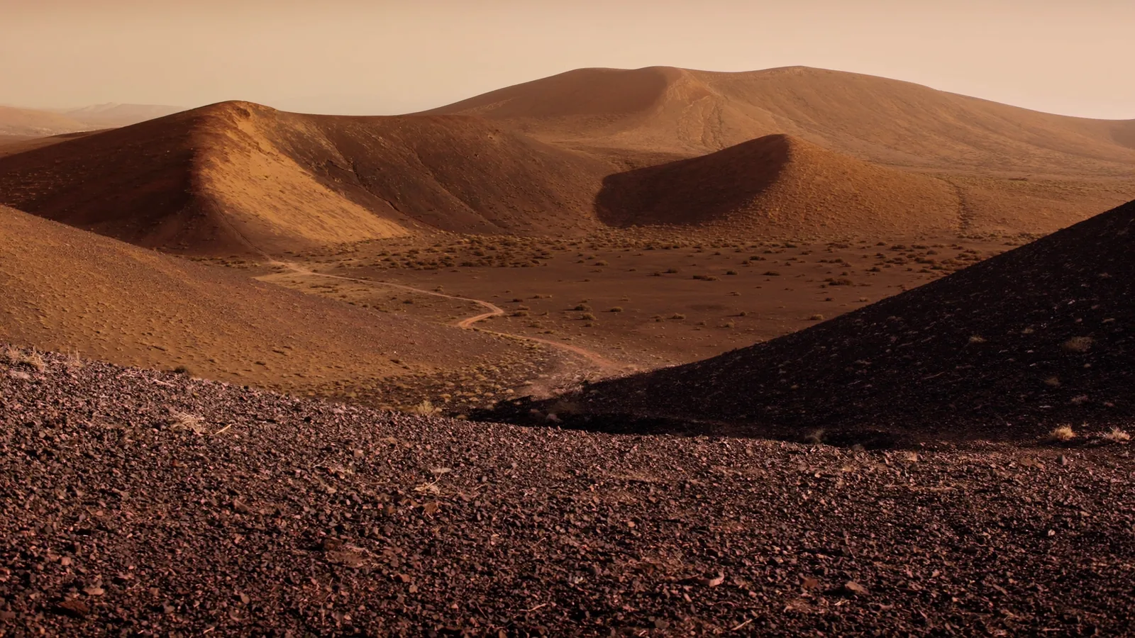 Visualización artística de conos volcánicos y una pista de tierra bajo una luz cálida de tarde