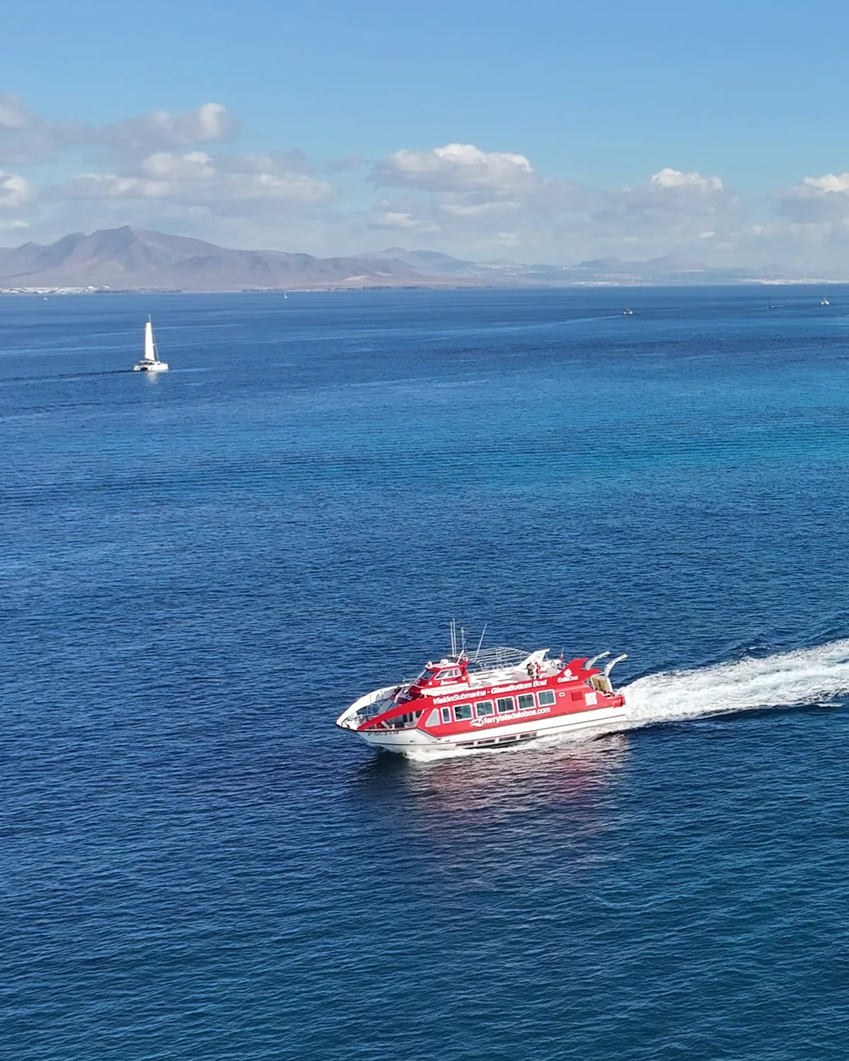 Minicrucero Celia Cruz de Grupo Oby navegando con su estela blanca sobre el mar azul, con las montañas de Lanzarote al fondo